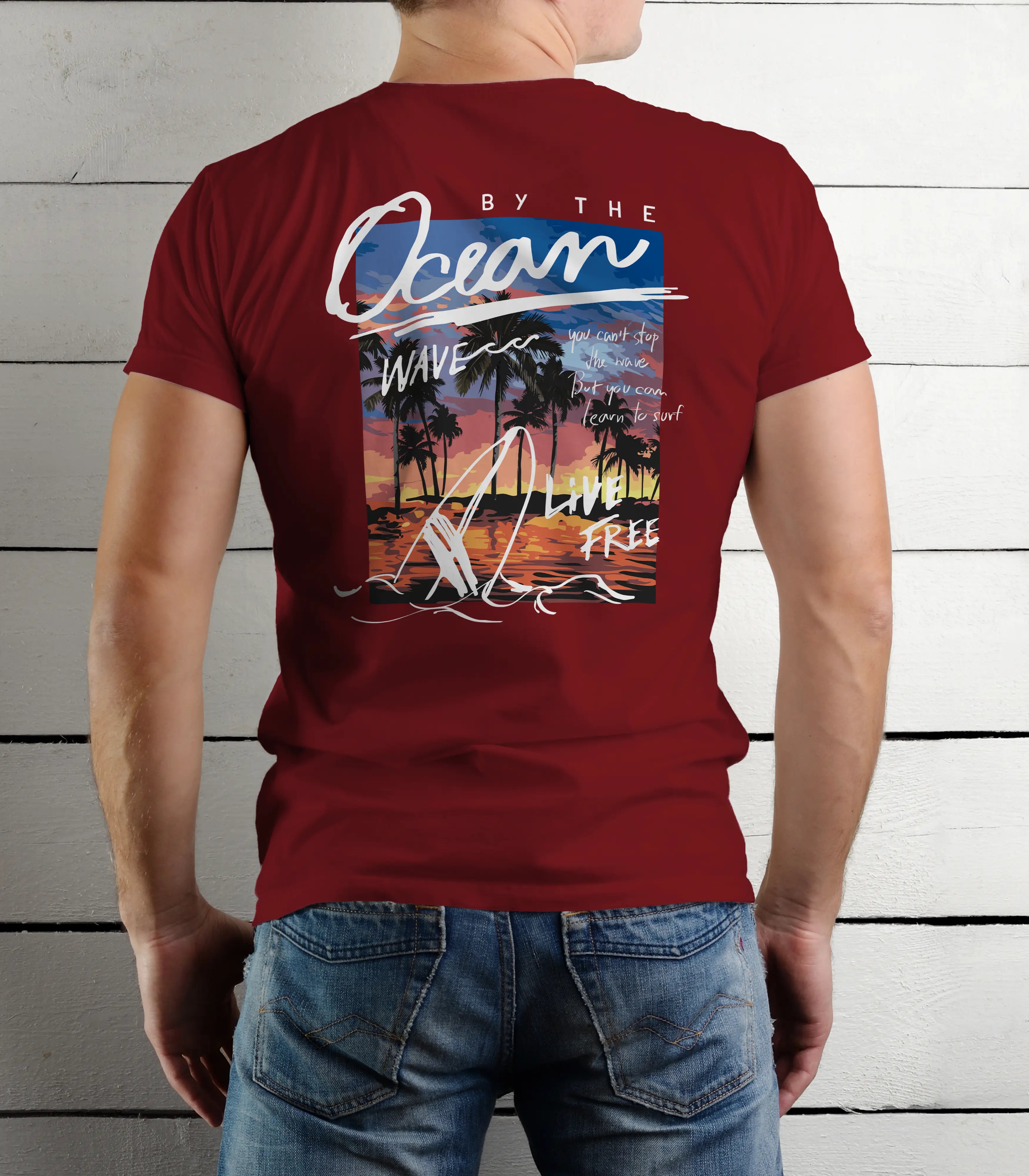 Person wearing a maroon t-shirt with a beach-themed design on the back, standing against a wooden panel background.