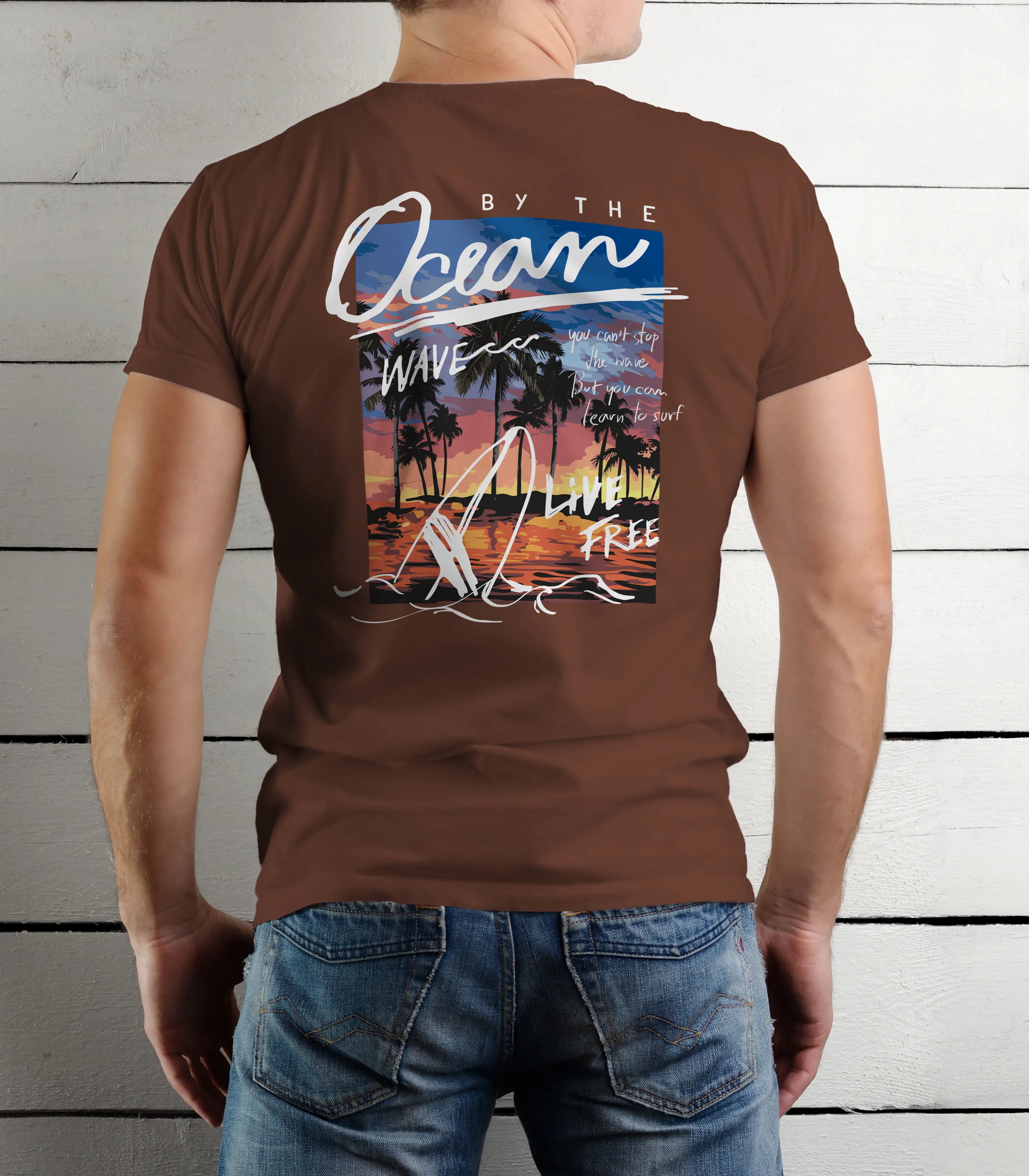 Person wearing a brown t-shirt with a beach-themed design on the back, standing against a wooden panel background.